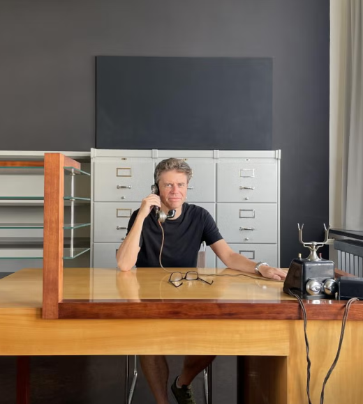 Man sitting at a large desk, answering an old fashioned phone