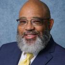 Bearded man in navy suit and yellow tie