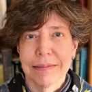 Woman wearing a floral scarf, standing in front of a bookcase