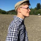 Person in page boy hat in front of a field